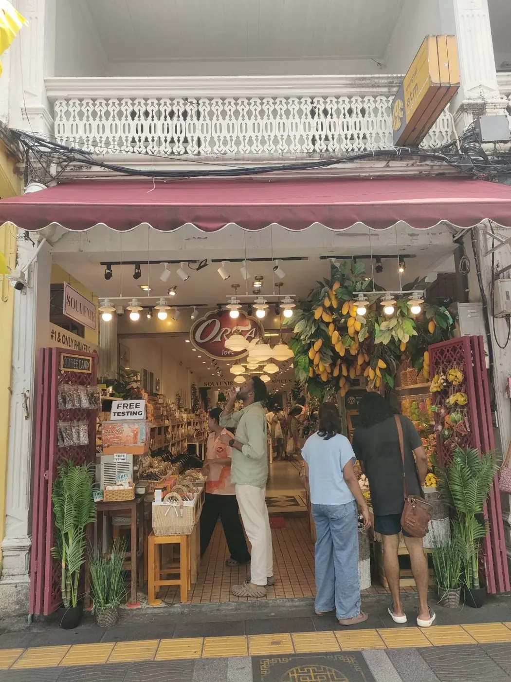 Visitors browsing a shop under a scalloped awning in Phuket Old Town